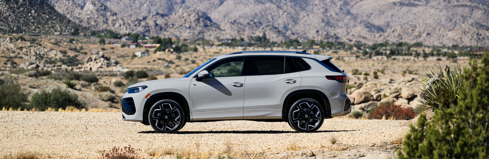 Vue latérale du Volkswagen Tiguan 2025 blanc stationnée sur une route pittoresque avec des collines en arrière-plan.